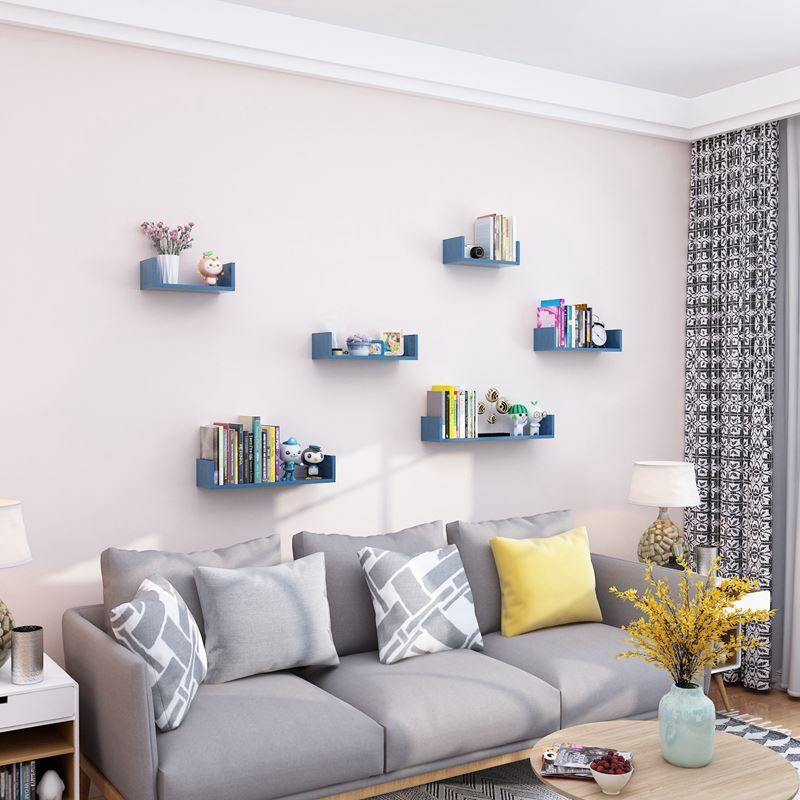 Blue wooden hanging shelves with books and decor in living room above gray sofa